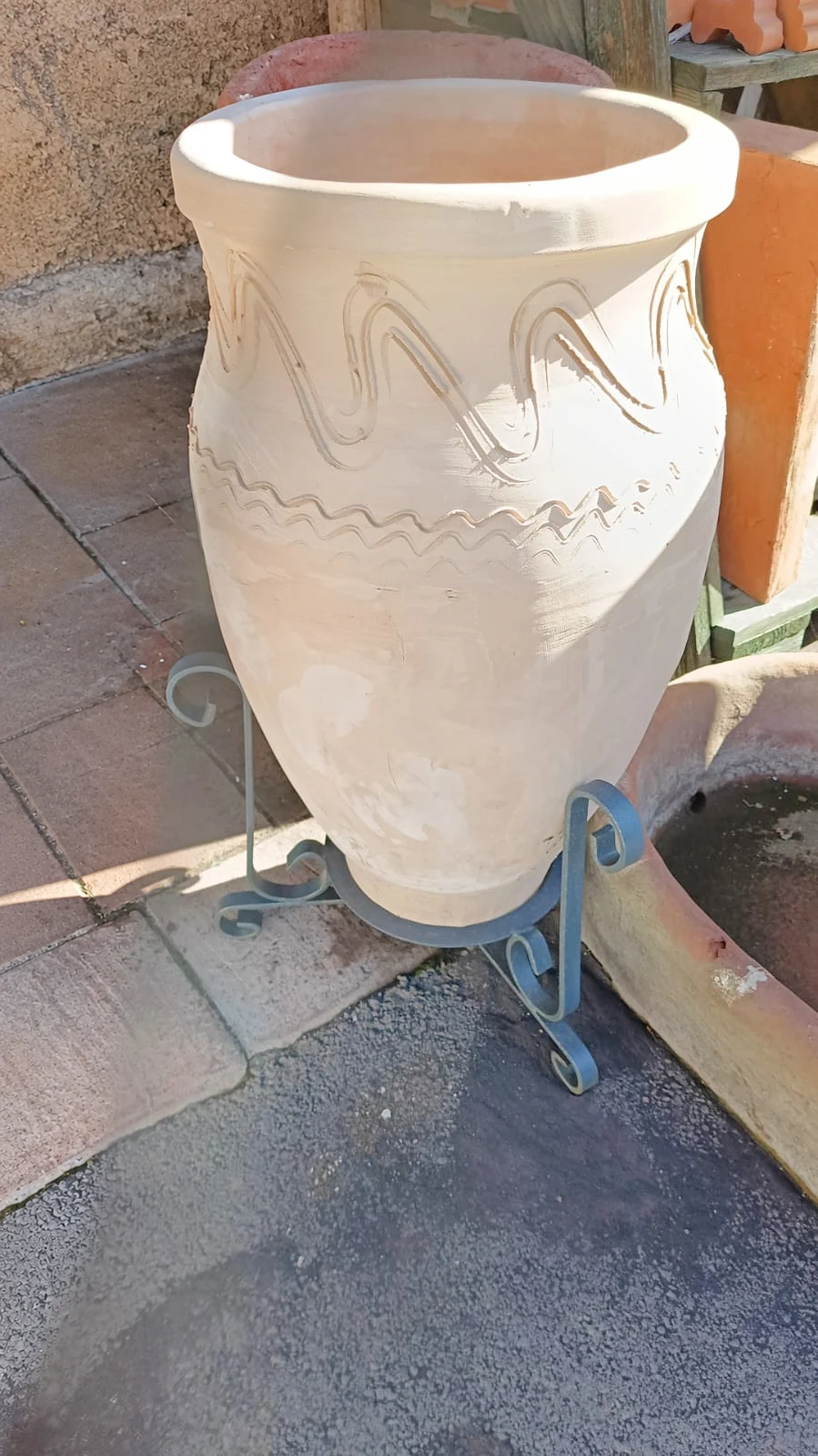 Una giara siciliana in terracotta chiara sul suo supporto in ferro